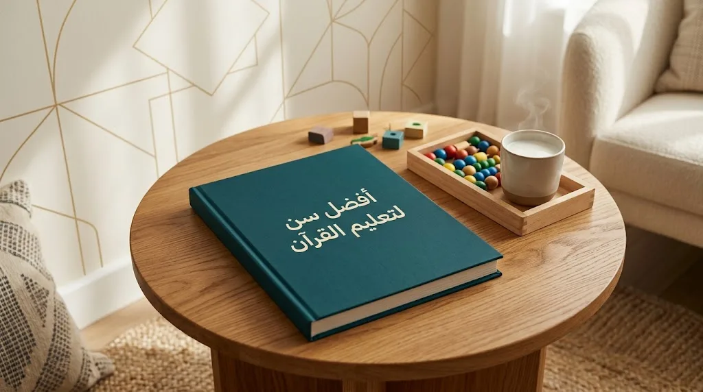 Teal hardcover book with an Arabic title on a round oak table beside a wooden tray of counting beads and a cup of milk